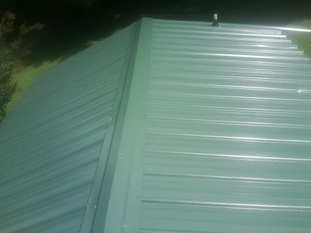New green metal panels meeting at the ridge of a roof — Flat Roof Repair work by our crew in Detroit