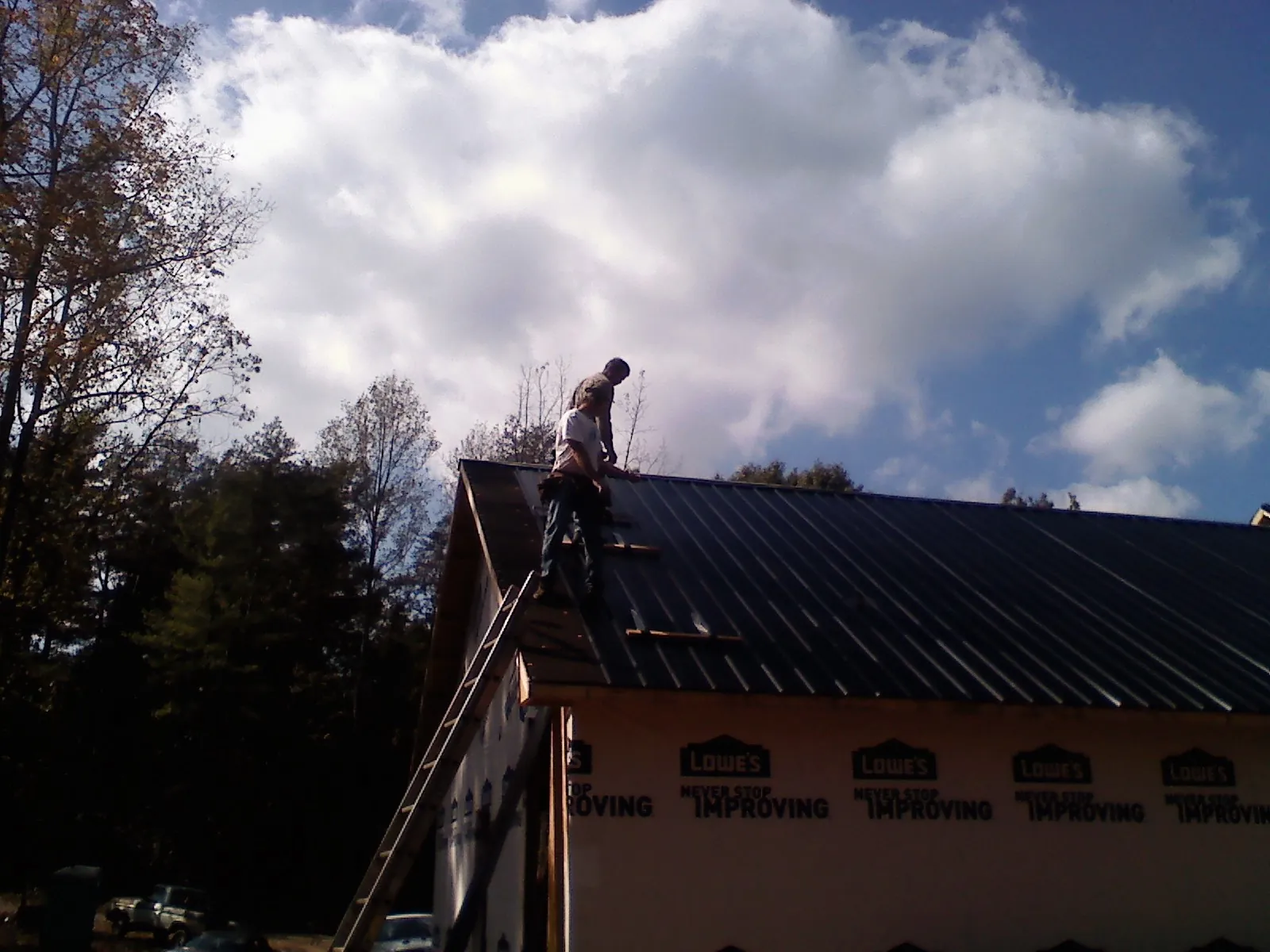 Roofer fastening dark metal panels high against a cloudy sky, from a Roof Inspection job in Detroit